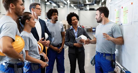 Young factory worker holding presentation about production development to company managers and his coworkers.